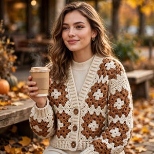 May include: A crochet cardigan featuring a granny square pattern in alternating cream and brown yarn. The garment has a V-neckline, long sleeves, and a front button closure with three brown buttons. It is worn over a cream-coloured ribbed shirt.