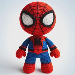 May include: A crocheted Spider-Man doll. The doll has a red head with a black web design and large white eyes. The body is blue with red details and a black spider emblem. The arms and legs are red, and the doll is standing. A handmade item.