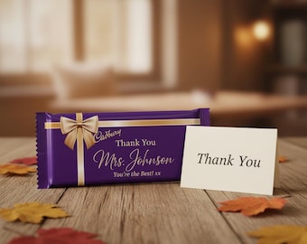 May include: A purple Cadbury chocolate bar wrapper featuring a gold ribbon graphic, the text Thank You Mrs. Johnson You're the Best! xx, and a small white folded card with the text Thank You printed in black on the front of the card.
