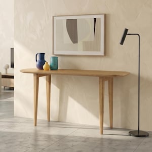 May include: A light wood console table with four tapered legs stands against a textured beige wall. On the table are three ceramic vessels in blue, yellow, and teal. Above the table hangs a framed abstract print with dark and light shapes.