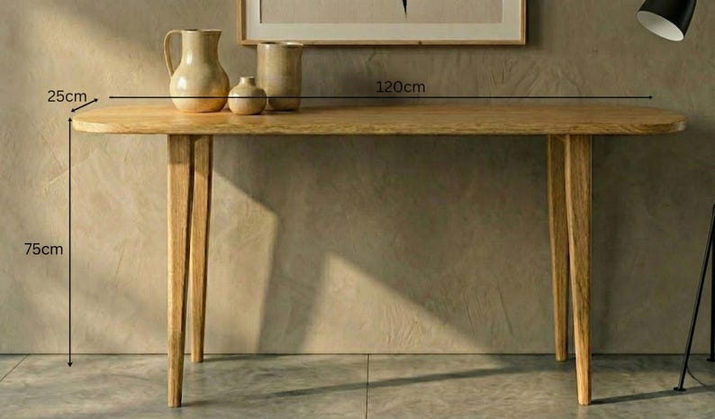 K&ouml;nnte beinhalten: Ein hellbrauner Holzkonsolentisch mit vier konisch zulaufenden Beinen und einer glatten, abgerundeten rechteckigen Tischplatte. Der Tisch ist 120 cm lang, 25 cm tief und 75 cm hoch. Drei Keramikvasen in verschiedenen Gr&ouml;&szlig;en stehen auf der Tischplatte.