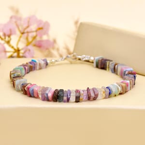 May include: A multi-coloured gemstone bracelet with square-cut stones in pink, purple, blue, and brown. The bracelet is strung on a silver chain and has a lobster clasp. A lovely piece of jewellery.