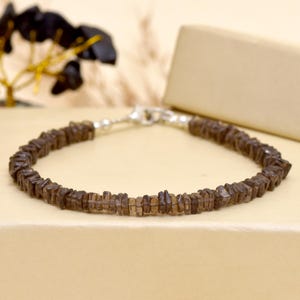 Peut inclure: Un bracelet composé de petites pierres précieuses marron de forme irrégulière. Le bracelet est fermé par un fermoir argenté. Les pierres sont enfilées pour former un bracelet continu. Présenté sur une surface neutre.