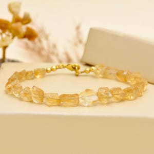 Puede incluir: Un brazalete de piedras preciosas de citrino con un cierre dorado. El brazalete presenta piedras de citrino en bruto e irregulares en tonos amarillos y ámbar. El cierre dorado y las cuentas de conexión añaden un toque de elegancia.