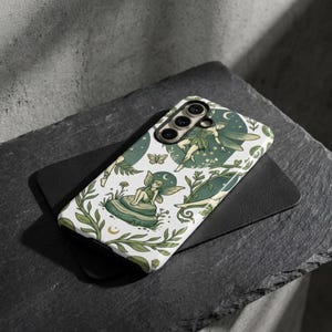 Puede incluir: Una taza de cerámica blanca con un asa negra y el texto "But First, Coffee" en negro, con una fuente de estilo manuscrito. La taza está sobre una superficie blanca.