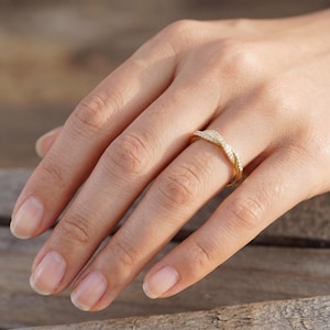 May include: A gold-colored ring with a twisted design, adorned with small, sparkling stones. The ring is worn on a finger, showcasing its intricate details and elegant style. The ring's design is a continuous loop, creating a flowing, eye-catching look.