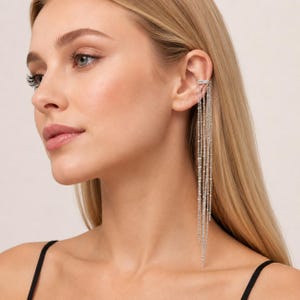 May include: A silver ear cuff featuring multiple delicate dangling chains of varying lengths. The metallic chains are attached to a small, circular ear cuff that secures to the upper cartilage, creating a cascading effect along the side of the ear.