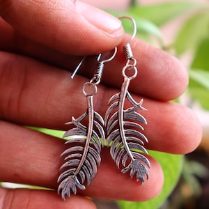 May include: A pair of silver feather earrings. Each earring features a detailed feather design with intricate lines and a textured surface. The earrings are suspended from a simple hook and coil design.