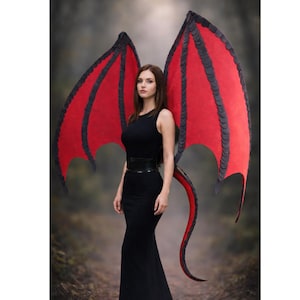 Könnte beinhalten: Eine Person in einem schwarzen Kleid mit großen roten und schwarzen Drachenflügeln und einem passenden Schwanz. Die Flügel sind weit ausgebreitet, und der Schwanz krümmt sich hinter ihr. Der Hintergrund ist eine verschwommene Waldszene.