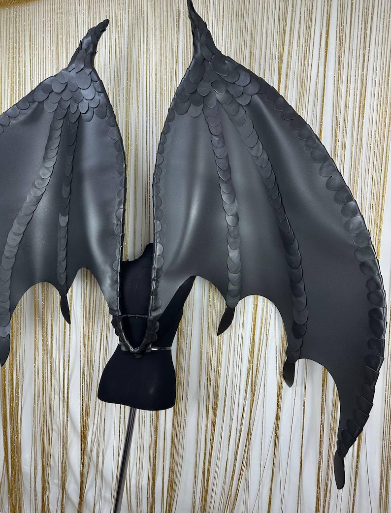 Puede incluir: Un par de alas de drag&oacute;n negras, grandes, con una apariencia texturizada y escamosa. Las alas est&aacute;n unidas a un arn&eacute;s negro, dise&ntilde;ado para ser usado. Las alas tienen puntas puntiagudas y una forma curva, para cosplay.