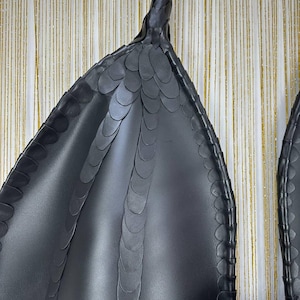 Puede incluir: Primer plano de un par de alas de drag&oacute;n negras de cuero sint&eacute;tico. Las alas tienen un patr&oacute;n texturizado en forma de escamas y una punta afilada. Estas alas est&aacute;n dise&ntilde;adas para ser usadas, probablemente como parte de un disfraz o cosplay.