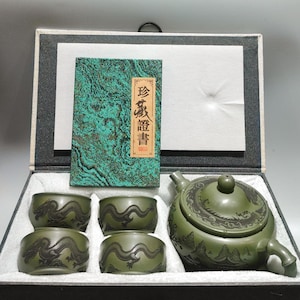 May include: A green ceramic tea set featuring a teapot and four matching cups, each decorated with embossed dragon motifs. The set is presented in a black box with a green textured certificate card featuring the Chinese characters 珍藏證書.