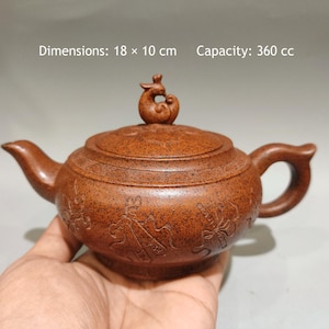 Puede incluir: Una tetera de arcilla marrón moteada con superficie texturizada, que presenta un remate de tapa con forma de ave y patrones grabados en el cuerpo. La tetera mide 18 x 10 cm con una capacidad de 360 cc, según el texto en la imagen.