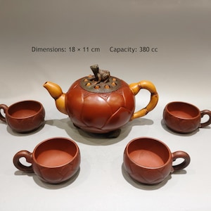 Könnte beinhalten: Eine braune Tonteekanne mit einem froschförmigen Deckelknauf, einem bambusartigen Griff und vier passenden Tassen. Das Set zeigt Lotusblütenblatt-Motive. Die Maße 18 x 11 cm und ein Fassungsvermögen von 380 cc sind auf dem Bild angegeben.