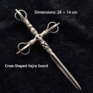 May include: A metallic cross-shaped Vajra sword with an intricate handle and a pointed blade. The object features a central hub with carved details and four looped prongs. The text reads: Dimensions: 28 x 14 cm and Cross-Shaped Vajra Sword.