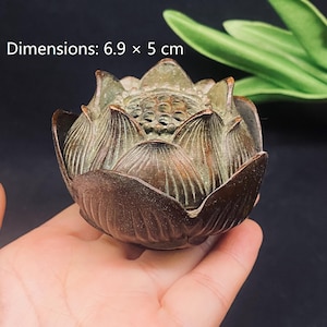 Puede incluir: Un quemador de incienso de metal color bronce con forma de flor de loto en flor con un acabado de pátina oscura texturizada. La parte superior presenta un diseño de vaina de semillas perforada. El objeto mide 6,9 por 5 cm según el texto.