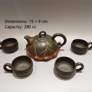 May include: A dark green ceramic tea set consisting of one teapot and four cups. The teapot features a leaf-shaped design with orange vein details, a curved handle, and a lid. Dimensions: 15 x 9 cm. Capacity: 280 cc. The cups have matching handles.
