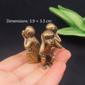 May include: A brass-colored metal figurine depicting three monkeys in the see-no-evil, hear-no-evil, and speak-no-evil poses. The monkeys are joined together in a circular formation. The text Dimensions: 3.9 x 3.3 cm is visible in the image.