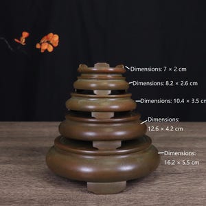 May include: A stack of five circular brown wooden display stands with varying diameters. The dimensions are labeled as 7 x 2 inches, 8.2 x 2.6 inches, 10.4 x 3.5 inches, 12.6 x 4.2 inches, and 16.2 x 5.5 inches for each individual stand.