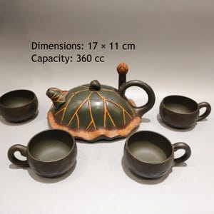 Puede incluir: Un juego de té de cerámica verde oscuro que incluye una tetera con forma de hoja de loto con vetas naranjas, una tapa con asa en forma de capullo y tres tazas a juego. La tetera mide 17 x 11 cm y tiene una capacidad de 360 cc.