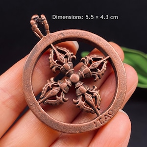 May include: A copper-coloured metal pendant featuring a circular frame enclosing a four-pronged vajra symbol. The pendant includes a top bail for hanging and has the text ITAO embossed on the lower rim. The dimensions are 5.5 x 4.3 cm.