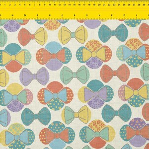 Puede incluir: Un patrón de tela con diseños de lazo de colores. Los lazos son en tonos de amarillo, naranja, azul, morado y verde, sobre un fondo crema. Los lazos están dispuestos en un patrón repetitivo.