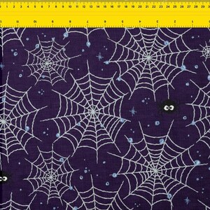 Pode incluir: Tecido roxo escuro com um padrão repetido de teias de aranha brancas, pequenos pontos azuis e estrelas. Uma aranha preta com olhos arregalados é visível. Este tecido com tema de Halloween é ideal para artesanato e costura.