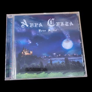 May include: A CD case featuring the album "Anna Celta" by Victor Santal. The cover art depicts a nighttime landscape with a castle, trees, a full moon, and stars. The text is in a stylized font, with a dark blue and purple color scheme.