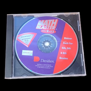 May include: A Math Blaster CD-ROM in a clear plastic case. The disc is purple and red, with text that reads "Math Blaster" and "Ages 9-12." It also states "Master Math for 4th, 5th & 6th Grades."
