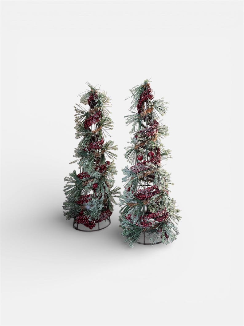Peut inclure: Deux arbres de No&euml;l d&eacute;coratifs. Chaque arbre est une armature m&eacute;tallique recouverte de fausses aiguilles de pin vertes, de baies rouges et d'une fine couche de neige blanche. Les arbres sont sur fond blanc.