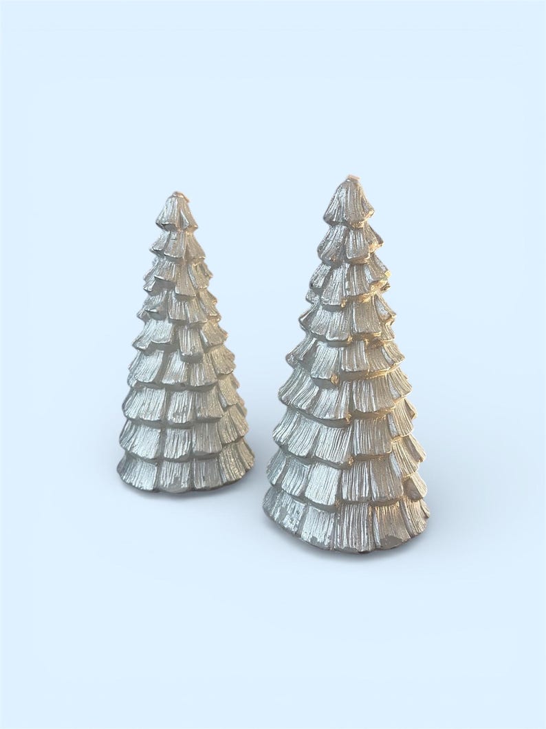 Peut inclure: Deux figurines argent&eacute;es en forme de sapin de No&euml;l textur&eacute;s. Les arbres ont un design en couches, chaque couche ressemblant &agrave; des branches. Les figurines sont pos&eacute;es sur un fond bleu clair, cr&eacute;ant un th&egrave;me festif et d&eacute;coratif.