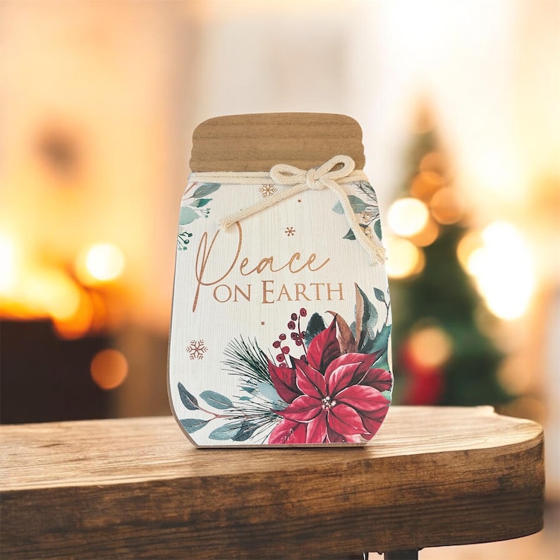 Peut inclure: D&eacute;coration en bois en forme de bocal Mason avec un couvercle marron et un n&oelig;ud en ficelle. Le bocal porte l'inscription &laquo; Peace on Earth &raquo; avec des motifs floraux et des flocons de neige, dont un poinsettia rouge.