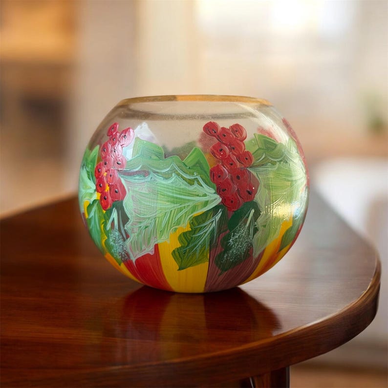 Peut inclure: Un bol en verre transparent avec un motif peint de baies rouges et de feuilles vertes. Le bol a une forme arrondie et repose sur une surface en bois. Le motif comprend des rayures jaunes et rouges.