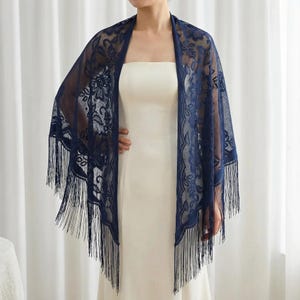 Może przedstawiać: Granatowa koronkowa szal z kwiatowymi wzorami i frędzlami. Szal jest narzucony na białą sukienkę, tworząc elegancki i wyrafinowany wygląd. Delikatny koronkowy wzór dodaje odrobinę kobiecości i uroku.