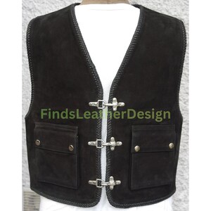 May include: A black suede vest featuring a braided trim along the edges, three silver-toned metal hook-and-eye closures down the front, and two front pockets with metallic snap buttons. The text FindsLeatherDesign is visible on the vest.