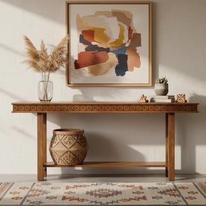 May include: A wooden console table with a woven basket, a framed abstract painting, and a patterned rug. The table has a decorative border and a lower shelf. A clear glass vase with dried plants and a small potted plant are on the table.