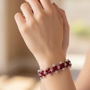 May include: A red and silver bracelet with a repeating floral design. The bracelet features small, round, red beads and silver-colored accents. The bracelet is worn on a wrist.