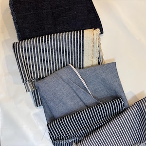 Könnte beinhalten: Ein Stapel aus fünf Stoffproben in verschiedenen Blautönen und Weiß. Die Proben sind gestreift und einfarbig und liegen auf einer weißen Oberfläche übereinander.