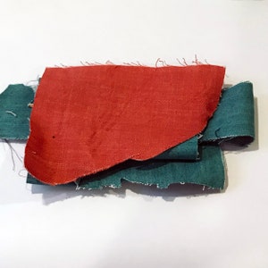 May include: A collection of fabric swatches in shades of teal and rust-orange. The pieces have raw, frayed edges, suggesting they are samples or remnants. The arrangement is layered, with the colors contrasting against each other.
