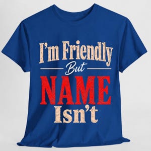 May include: A royal blue short-sleeve t-shirt featuring the text "I'm Friendly But NAME Isn't" printed on the front. The words "I'm Friendly" and "Isn't" are in a distressed beige font, while the word "NAME" is in a large, bold, distressed red font.
