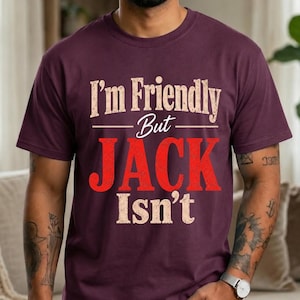 May include: A dark maroon short-sleeve t-shirt featuring the text "I'm Friendly But JACK Isn't" printed on the front. The words "I'm Friendly But" and "Isn't" are in a distressed beige font, while the word "JACK" is in a bold, distressed red font.
