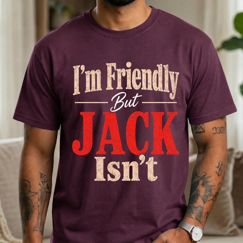 May include: A dark maroon short-sleeve t-shirt featuring the text "I'm Friendly But JACK Isn't" printed on the front. The words "I'm Friendly But" and "Isn't" are in a distressed beige font, while the word "JACK" is in a bold, distressed red font.