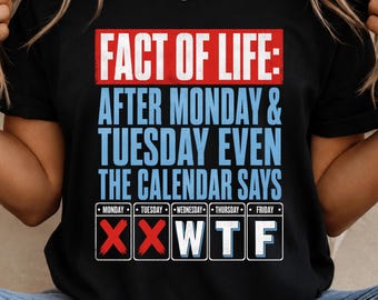 May include: A black short-sleeved t-shirt featuring a graphic print with the text "FACT OF LIFE: AFTER MONDAY & TUESDAY EVEN THE CALENDAR SAYS" in white and light blue, followed by a calendar row with red X marks over Monday and Tuesday.