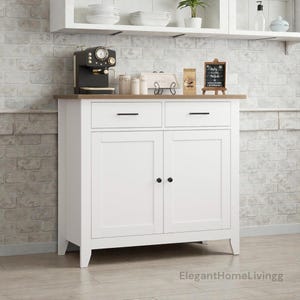 May include: A white cabinet with two doors and two drawers, topped with a brown surface. A black espresso machine, jars, and a small chalkboard sign are on top. The cabinet is in a kitchen setting.