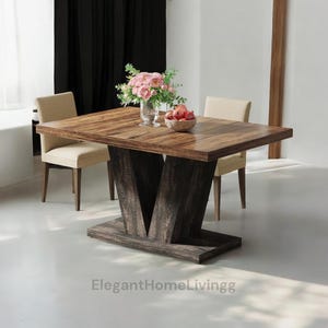 May include: A rectangular wooden dining table with a dark brown finish, supported by a dark gray, V-shaped base. Two beige chairs are positioned on either side. The table is decorated with a vase of pink flowers and a bowl of red fruit. The text "ElegantHomeLivingg" is at the bottom.