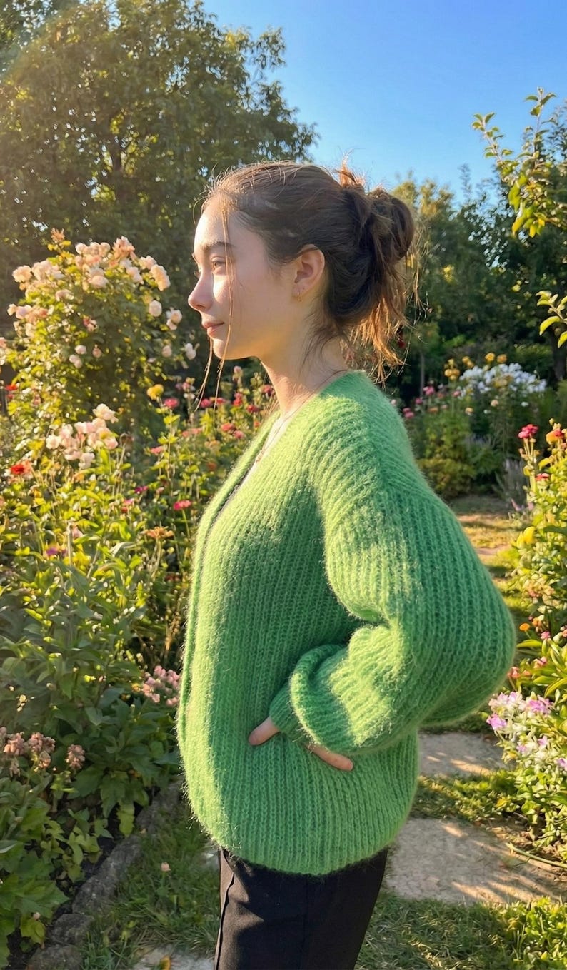 May include: A bright green, chunky knit cardigan. The sweater has a V-neck and long sleeves. The person is standing in a garden with flowers and greenery in the background.
