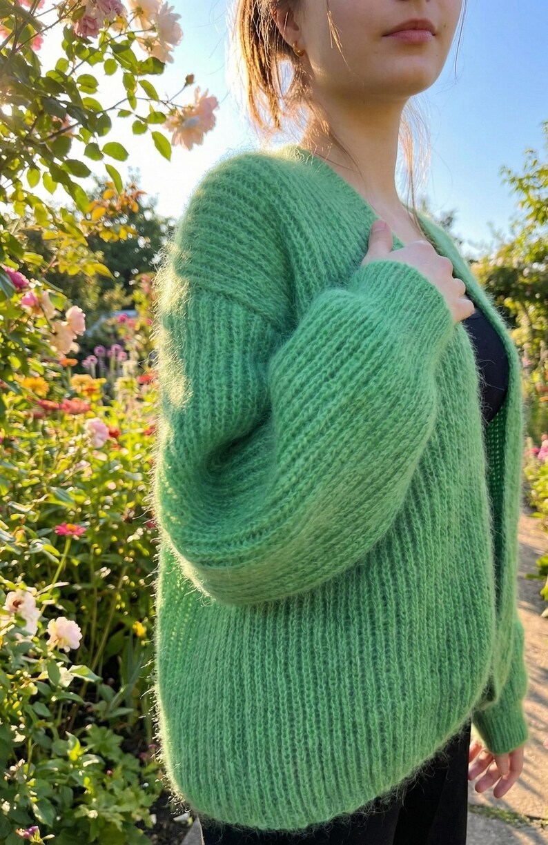 May include: A vibrant green, open-front cardigan made of a soft, textured knit. The long-sleeved sweater has a relaxed fit and is shown outdoors with a garden background. The cardigan is a solid color and has a V-neck.