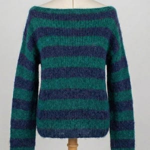 May include: A green and navy blue striped sweater with a boat neck. The long-sleeved sweater is displayed on a mannequin. The sweater's stripes are horizontal and evenly spaced, creating a classic and cozy look. The fabric appears soft and textured.