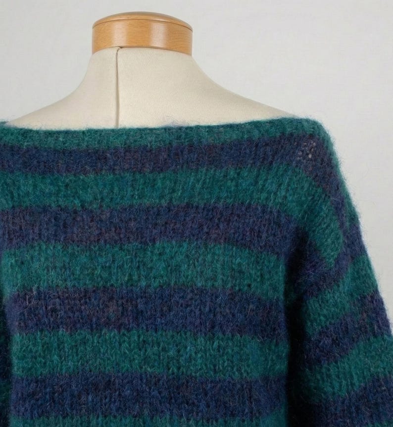 May include: A green and navy blue striped sweater with a boat neck. The sweater is made of a soft, textured material and is displayed on a mannequin. The stripes are horizontal and evenly spaced.