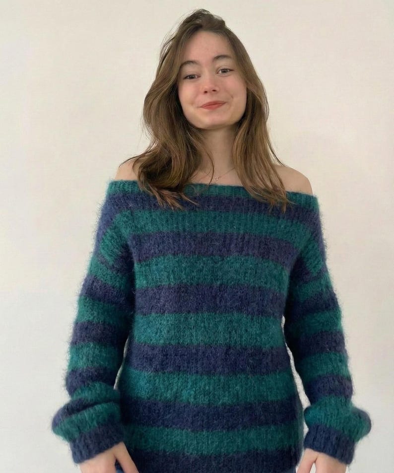 May include: Off-the-shoulder sweater with horizontal stripes in shades of teal and navy blue. The sweater has long sleeves and a soft, textured appearance. The model is wearing the sweater.